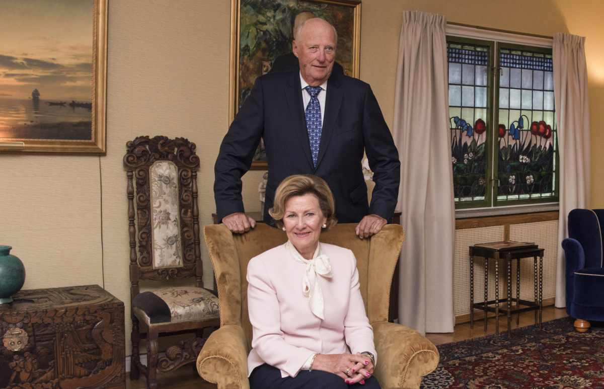 Norway's Queen Sonja sitting in a chair with King Harald standing behind in the living room of the Queen's childhood home at Maihaugen open-air museum in Lillehammer.