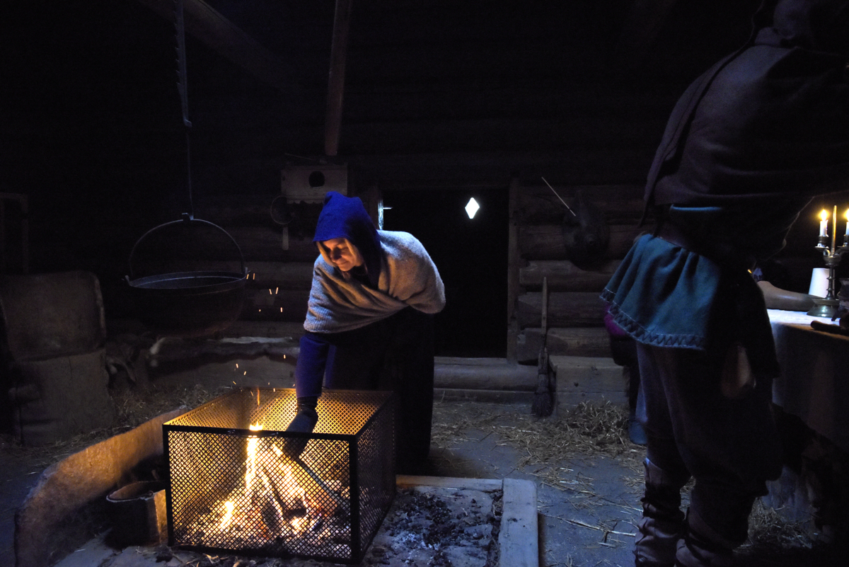 A woman lits the fire inside the open-hearth house. Photo: Camilla Damg&aring;rd/Maihaugen


