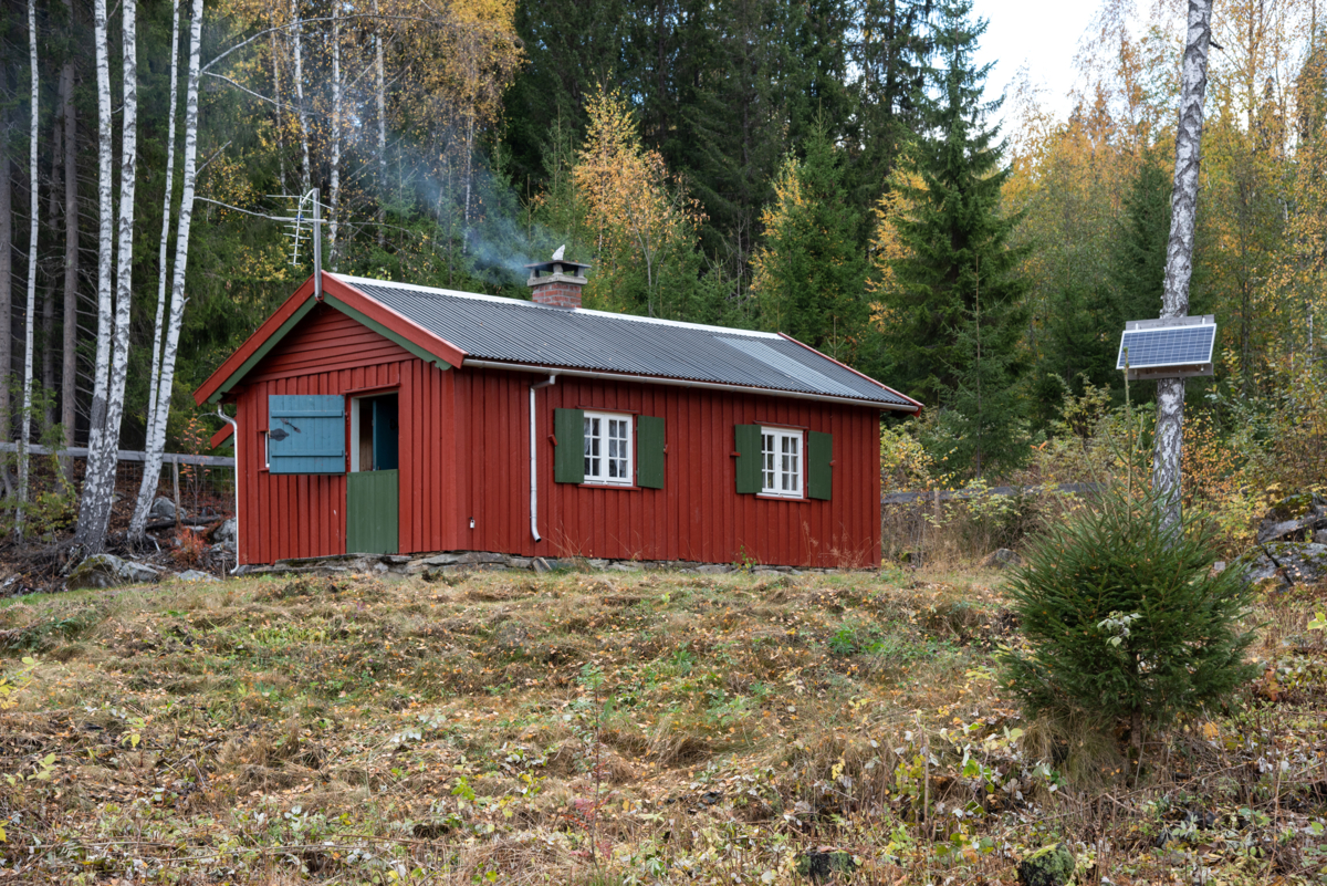 Red-painted cabin with white windows and green shutters.